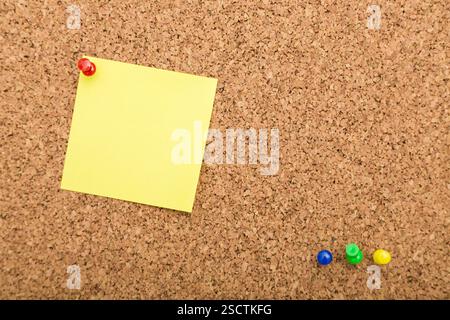 Yellow sticky note on corkboard with colored push pins arranged for task reminders or planning Stock Photo
