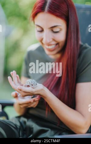 Young woman joyfully interacting with a small spotted lizard in a serene outdoor setting, highlighting a love for nature and an appreciation for Stock Photo