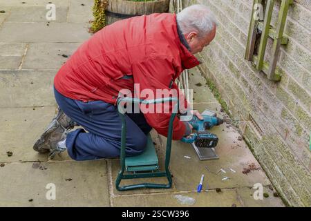 A male (man) using a cordless power drill to secure a cover over an air brick. The air brick cover is used for pest control to stop mice entering. Stock Photo