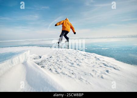 Man athlete in yellow jacket ice skating on frozen lake with cracks and snow at winter time Stock Photo