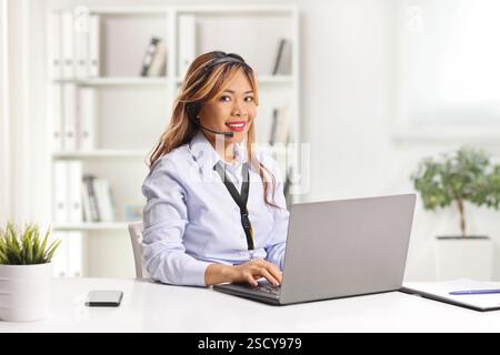Asian woman working on a laptop computer with wireless handsfree headphones in an office Stock Photo