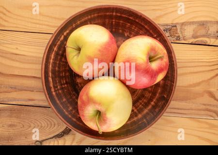 Three organic apples with a clay plate on a wooden table, close-up, top view. Stock Photo