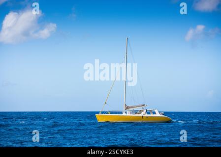 Yellow catamaran sailing on vivid blue Caribbean Sea on a sunny day with small puffy white clouds dotting the blue sky. Stock Photo