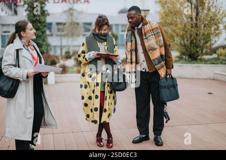 Three people collaborating outdoors in modern casual attire during autumn season Stock Photo