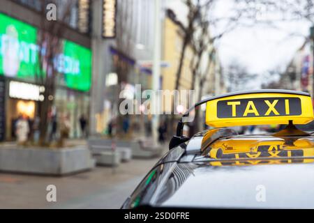 Bright yellow taxi cab with illuminated sign parked on a bustling city street surrounded by shops, buildings and pedestrians Stock Photo