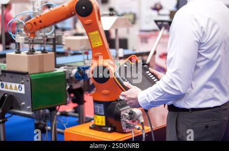 Engineer utilizing a control panel to operate a robotic arm in a automated industrial packing system Stock Photo