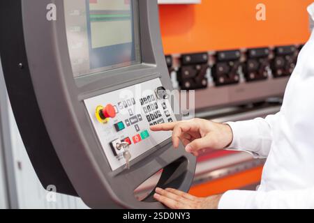 Professional operator interacting with a high-tech industrial CNC machine control panel, ensuring precision and efficiency in a modern manufacturing s Stock Photo