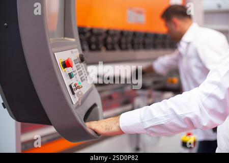 Professional operator interacting with a high-tech industrial CNC machine control panel, ensuring precision and efficiency in a modern manufacturing s Stock Photo