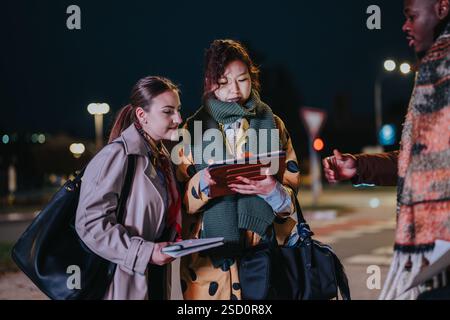 Multiracial businesspeople collaborating using a tablet outdoors at night in an urban setting Stock Photo