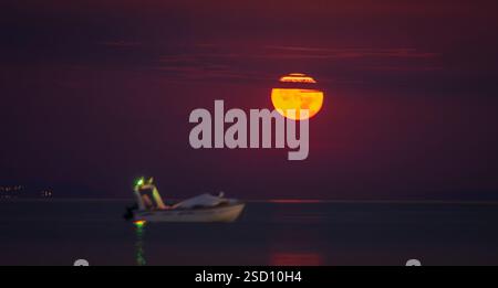 A boat is floating on the water with a full moon in the background. The moon is bright and the sky is dark, creating a serene and peaceful atmosphere Stock Photo