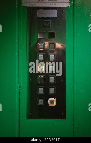 Metal elevator control panel with floor selection buttons, the eleventh floor is selected. The elevator cabin is green. Stock Photo