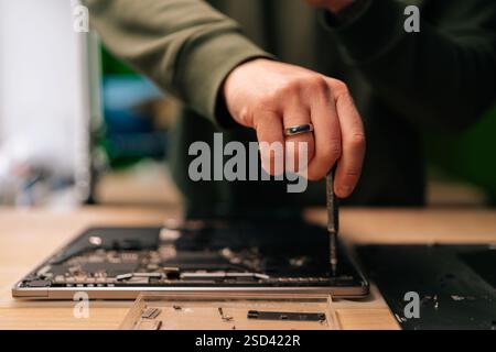 Close-up hands of unrecognizable computer master using screwdriver to repair motherboard of disassembled laptop in workshop. Stock Photo