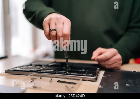 Cropped shot of electronics repair professional carefully disassembling laptop motherboard, precision screwdriver in hand, surrounded by various Stock Photo