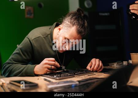 Portrait of electronic technician inspecting damaged laptop motherboard, diagnosing complex hardware malfunction sitting at table in professional Stock Photo