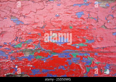 Colors of red, blue, and green blend together in a striking display of peeling paint on an old surface. The texture creates a sense of age and history Stock Photo