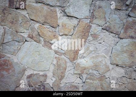 Close-up view of a natural stone wall featuring various shades and textures. The surface showcases unique patterns formed by the arrangement of differ Stock Photo
