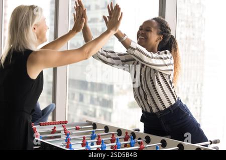 Colleagues playing table football, giving high five gesture, celebrate victory Stock Photo