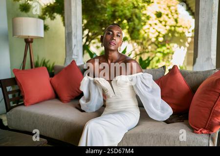 Person in white dress on villa couch. LGBTQ marriage concept. Tropical, luxury vibe. Inclusive wedding venue, welcoming atmosphere. Fashion, elegance Stock Photo