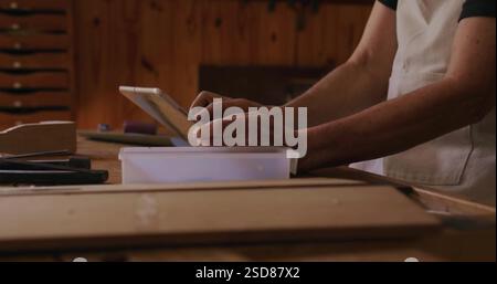 Carpenter using tablet in workshop, planning woodworking project with tools nearby Stock Photo