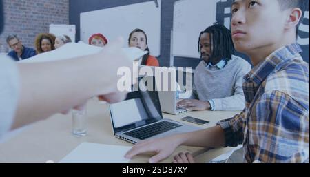 In office, diverse team collaborating on project with laptops and documents on table Stock Photo