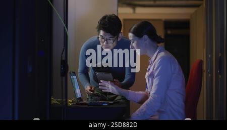 IT professionals collaborating on tablet and laptop in server room, focused on task Stock Photo