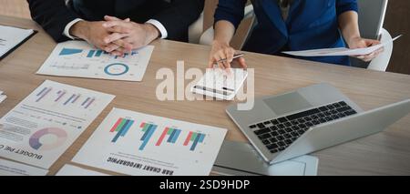 Close-up of diverse business team analyzing financial reports and using a calculator in a modern office. Stock Photo