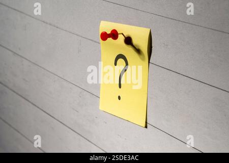 A yellow sticky note with a question mark written on it is pinned to a wooden board. Thinking, brainstorming concept. Stock Photo