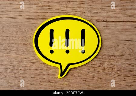 A yellow speech bubble with multiple exclamation marks on a wooden background. Warning, alert, caution concept. Stock Photo
