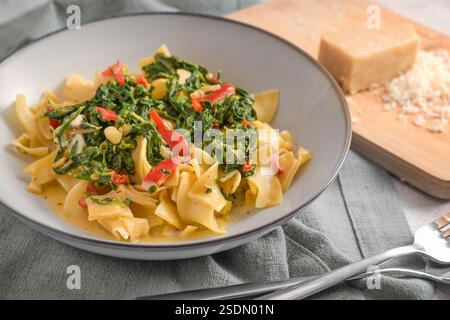 Tagliatelle with spinach and red bell pepper in a plate on a gray napkin, parmesan cheese on a cutting board, cooking a vegetarian pasta dish, selecte Stock Photo
