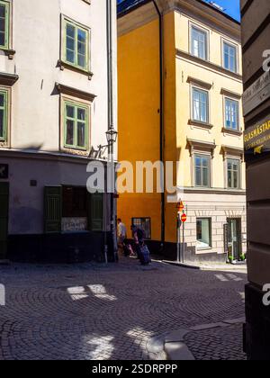 Cobblestone street corner in Stockholm's popular old town ('Gamla Stan') with colourful painted buildings and 2 tourists wheeling suitcases. Stock Photo