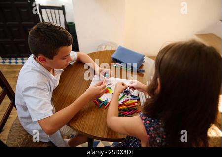 Two children are seen at a table collaborating on a creative drawing project, surrounded by colorful art supplies, fostering creativity and teamwork. Stock Photo
