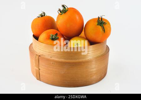 Collection of freshly picked ripe tomatoes arranged in a charming wooden basket, captured on a clean white backdrop Stock Photo