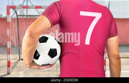 Cropped rearview image of a young player man holding a soccer ball under his arms wearing red shirt Stock Photo