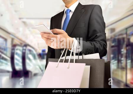 Cropped shot of shopper man holding the shopping bags an using the smart phone at the center mall. Concept of shopaholic man. Stock Photo