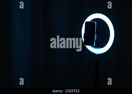 Glowing ring lamp with smartphone on black background. Space for text Stock Photo