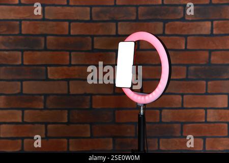 Ring lamp with smartphone against brick wall, space for text Stock Photo