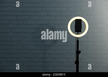 Ring lamp with smartphone against brick wall, space for text Stock Photo