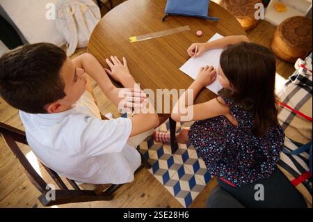 Two children sit at a table working on schoolwork together, showing teamwork. Stock Photo