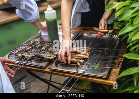 Chefs grilling seafood in an outdoor setting, preparing dishes for a wedding reception, with fresh ingredients and greenery surrounding the area Stock Photo