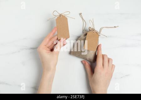 Woman with burlap bag and tags on white marble table, top view Stock Photo
