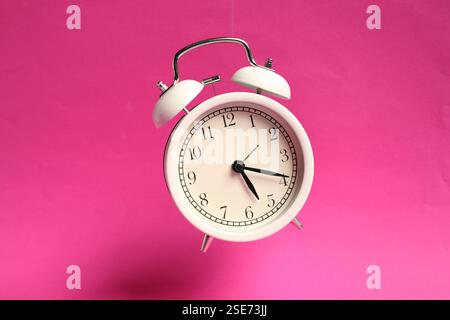 White alarm clock in air on bright pink background Stock Photo