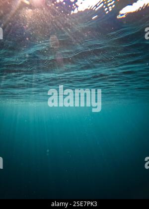 Deep blue underwater background with sunrays and reflections on the rippled water surface. Stock Photo