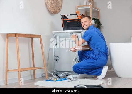 Male plumber repairing washing machine in bathroom Stock Photo