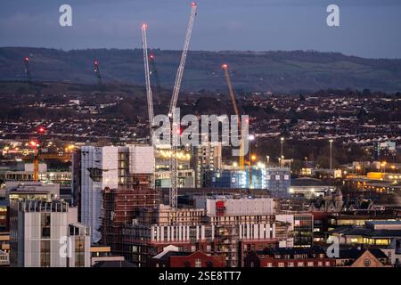 Construction cranes tower over building sites in the Redcliffe neighbourhood of Bristol at dusk, with Lansdown Hill on the Cotswold Edge rising in the Stock Photo
