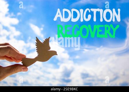 Addiction recovery symbol. Concept words Addiction recovery on beautiful blue sky. Psychologist hand, wooden bird. Beautiful blue sky cloud background Stock Photo
