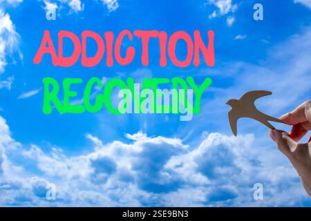 Addiction recovery symbol. Concept words Addiction recovery on beautiful blue sky. Psychologist hand, wooden bird. Beautiful blue sky cloud background Stock Photo