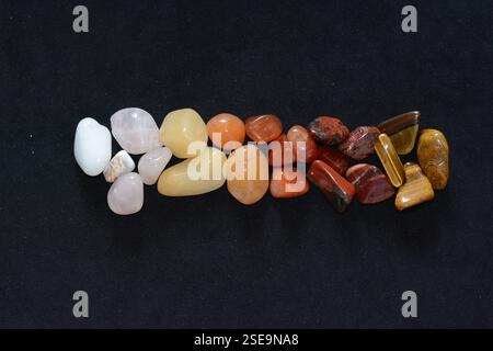 A variety of raw mineral gemstones in different shapes and colors, including quartz, agate, jasper, tiger eye arranged neatly on a black background Stock Photo