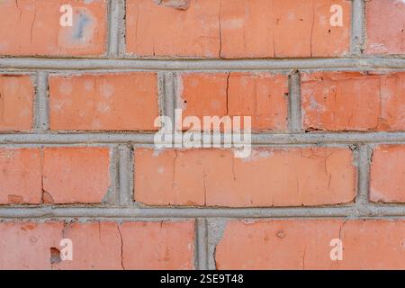 An aged red brick wall showcases visible cracks and worn mortar. The texture and color reveal the wall's history and exposure to the elements over tim Stock Photo
