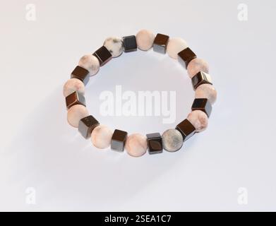 A vibrant close-up shot of a colorful gemstone bracelet featuring peach, brown, white, black, and gray quartz beads, set against a white background Stock Photo