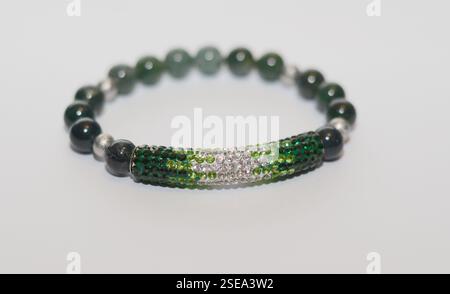 Elegant handmade beaded bracelet with dark green gemstones and a sparkling rhinestone-encrusted curved bar, set against a white background Stock Photo